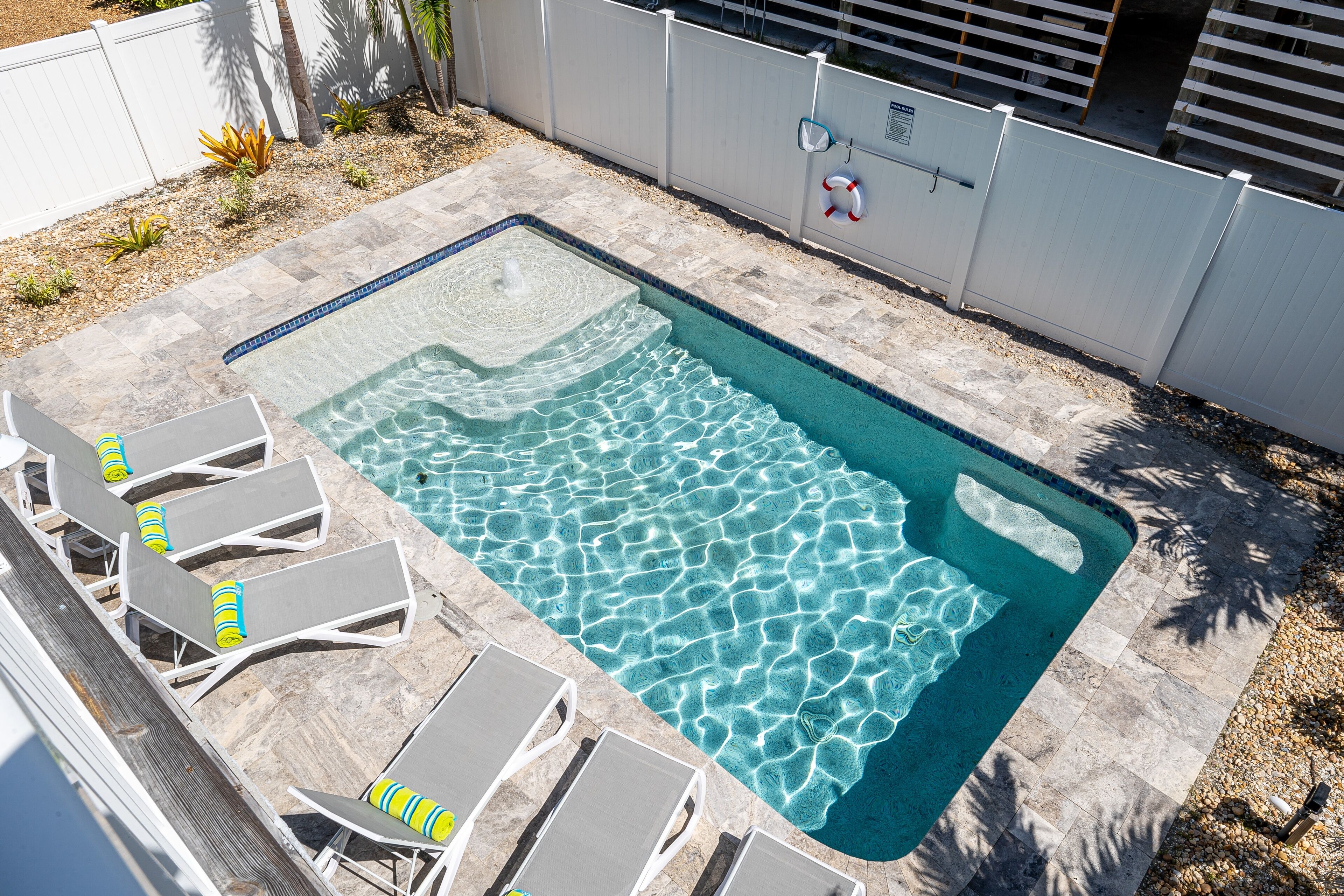 En rektangulær swimmingpool med klart vand, omgivet af en stengang og hvide liggestole.