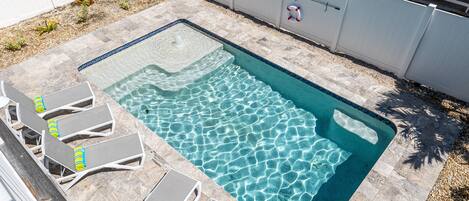 En rektangulær swimmingpool med klart vand, omgivet af en stengang og hvide liggestole.
