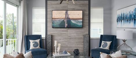 Una sala de estar moderna con un televisor grande, dos sillones, una mesita de centro y vistas al exterior.