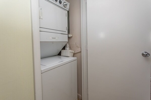 A compact laundry room with a washer and dryer, a small shelf, and a door.