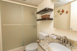 A bathroom with a toilet, sink, and shower. There are shelves above the sink with baskets and a mirror with decorative fish.