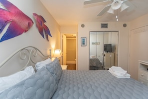 A hotel room with a bed, a ceiling fan, a mirror, and a wardrobe.