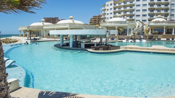 A resort pool with a bar area, lounge chairs, and a view of the ocean. - Stunning 4 Bedroom Beach Villa on Sandy Beach at Las Palmas Beachfront Resort V9 3 Villa by RedAwning (Puerto Peñasco)