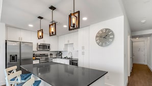 Une cuisine moderne dotée d’un îlot central, d’appareils électroménagers en acier inoxydable et de luminaires suspendus.