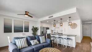 Un salon moderne avec un canapé, un pouf en osier et un coin repas agrémenté de tabourets de bar.