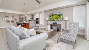 Una sala moderna con un sofá gris, un sillón estampado y un televisor en la pared.