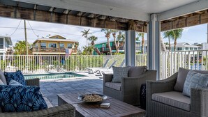 A covered outdoor area with wicker furniture, a pool, and a view of neighboring houses.