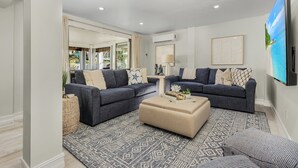 A modern living room with two dark sofas, a beige ottoman, and a patterned rug.