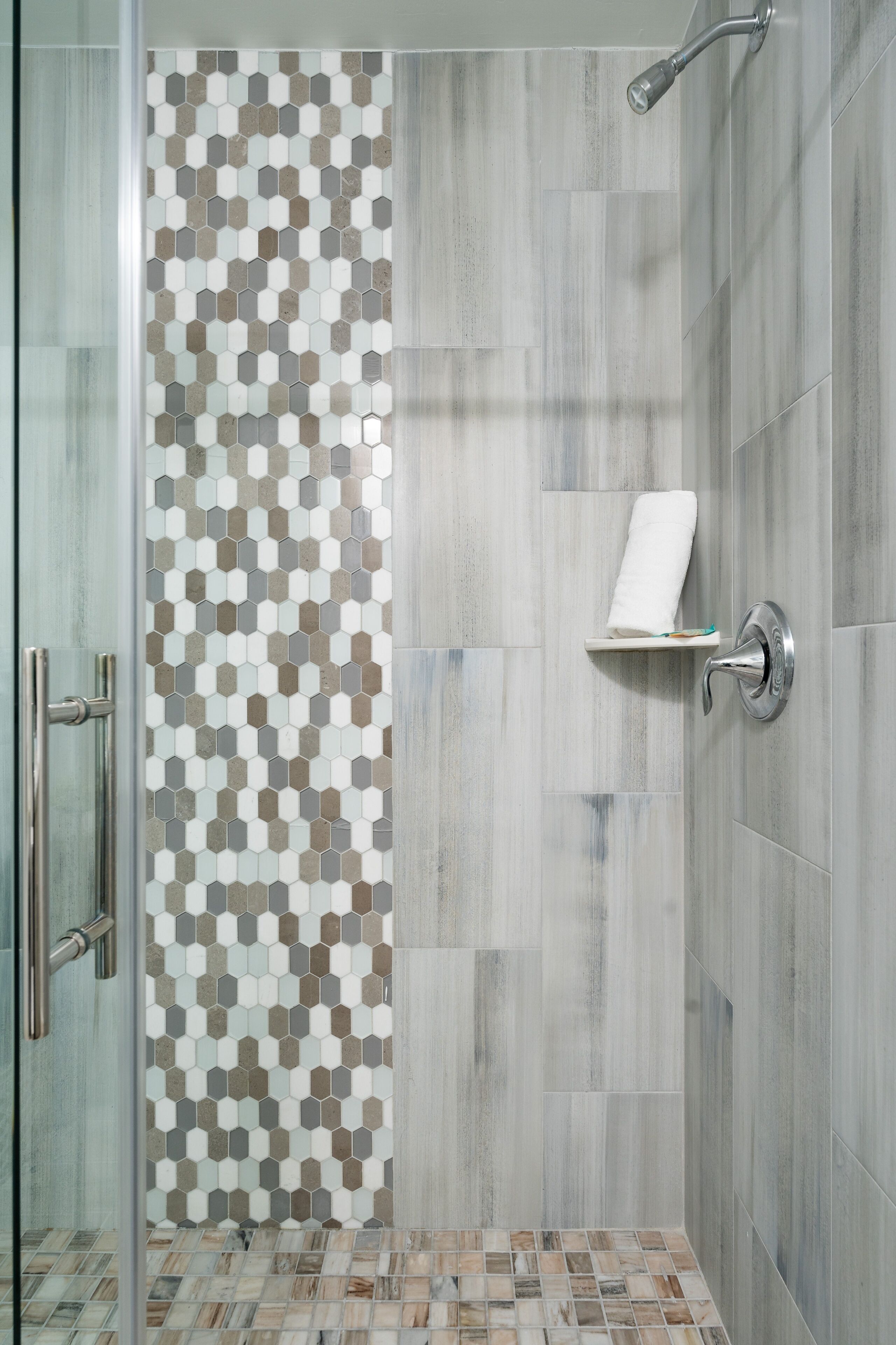 A shower with a glass door, a tiled wall with a geometric pattern, and a shelf with a towel.