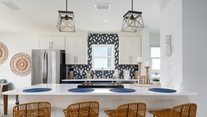 A modern kitchen with white cabinets, a stainless steel refrigerator, and a central island with four wicker chairs.
