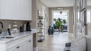 A modern kitchen with white cabinetry, a marble countertop, and a built-in sink. There is a black coffee machine and a vase on the counter. - Magnificent New Build Private Pool Home On The North Tip Of Fort Myers Beach! 5 Bedroom Home by RedAwning (Fort Myers Beach)