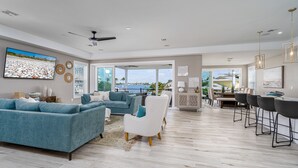 A spacious living area with a large TV, a ceiling fan, and a view to the outside. - Magnificent New Build Private Pool Home On The North Tip Of Fort Myers Beach! 5 Bedroom Home by RedAwning (Fort Myers Beach)