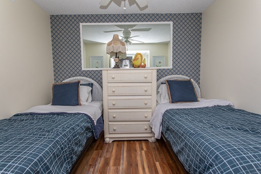 A bedroom with two beds, a dresser, a mirror, and a ceiling fan.