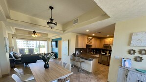 A spacious kitchen with a central island, a dining area with a wooden table and white chairs, and a living area with a sofa and chairs. - Beautiful 2 Bedroom Condo on the Sea of Cortez at Las Palmas Resort D-501 2 Condo by RedAwning (Puerto Peñasco)