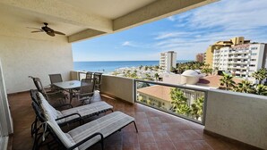 A balcony with a table and chairs, a ceiling fan, and a view of the ocean and buildings. - Beautiful 2 Bedroom Condo on the Sea of Cortez at Las Palmas Resort D-501 2 Condo by RedAwning (Puerto Peñasco)