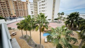 A hotel courtyard with palm trees, a pool, and a view of the ocean. - Beautiful 1Â½ Bedroom Condo on the Sea of Cortez at Las Palmas Resort D-304 2 Condo by RedAwning (Puerto Peñasco)