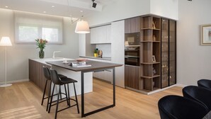 A modern kitchen with a central island, bar stools, a built-in oven, and a wooden cabinet with glass doors. - Villa Tereza (Zadar)