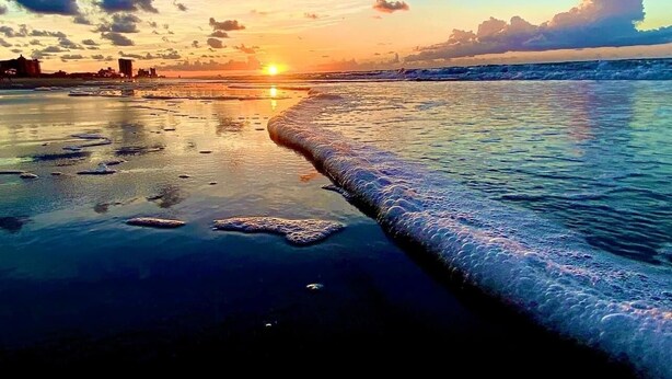 A beach scene with a sunset, waves, and a distant city skyline. - Your Personal Oceanfront Resort w/ Heated Pool SP (North Myrtle Beach)