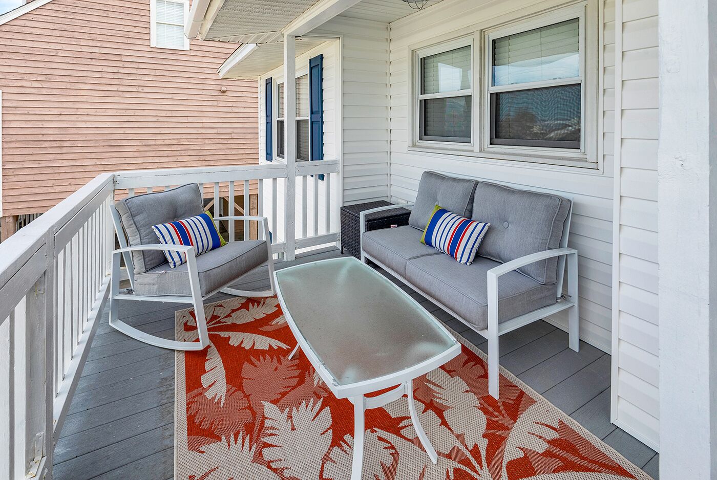 A covered porch with two gray sofas, a white table, and a red and white patterned rug.