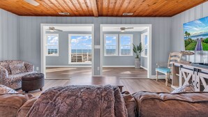A spacious living room with a wooden ceiling, large windows, a view of the ocean, a sofa, a chair, and a TV. - Your Personal Oceanfront Resort w/ Heated Pool SP (North Myrtle Beach)