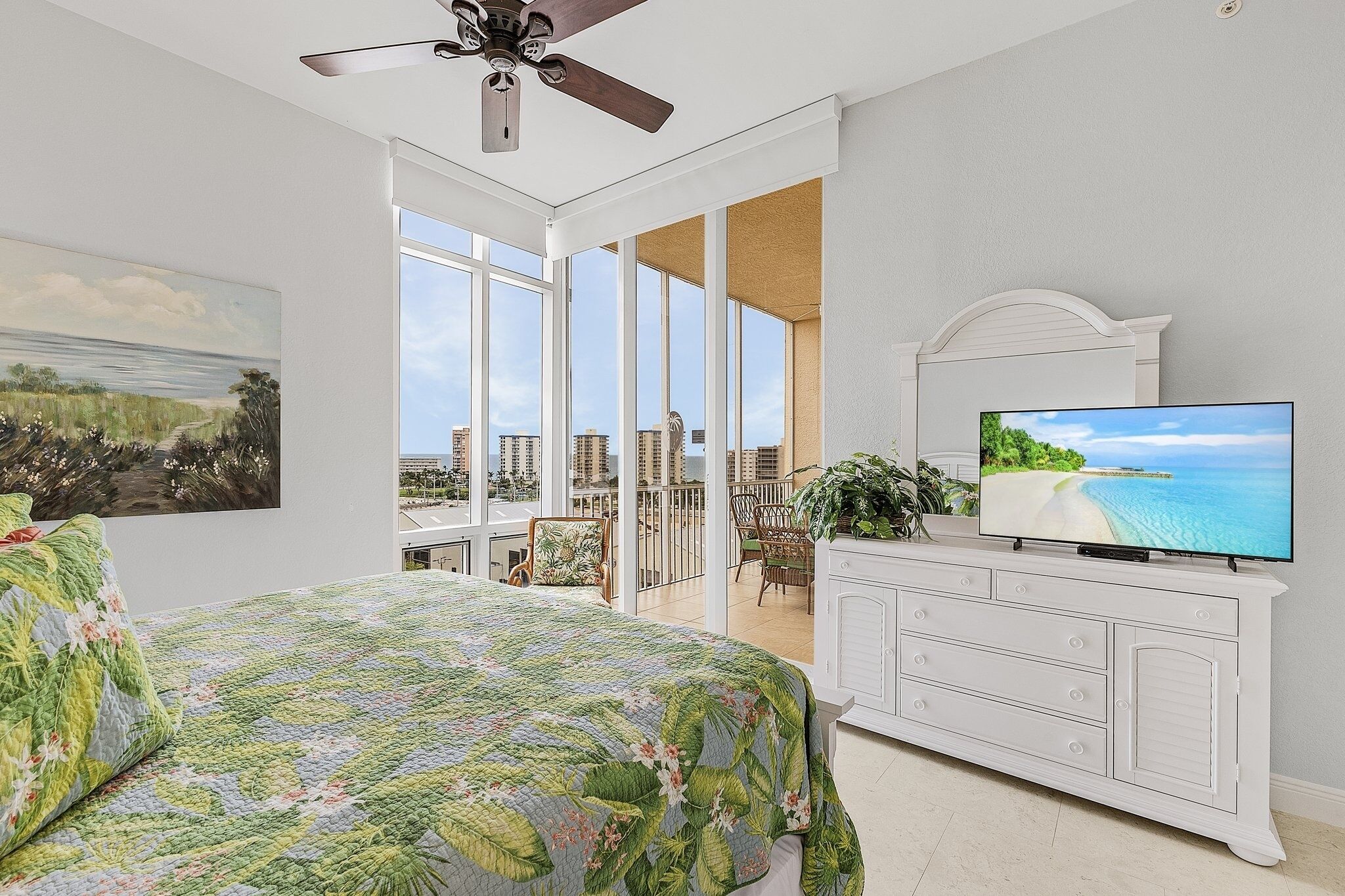 Ein Schlafzimmer mit einem großen Bett, einem Fernseher, einem Deckenventilator und einem Balkon mit Stadtblick.