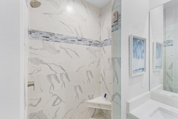 Un baño con baldosas de mármol, cabina de ducha de vidrio y lavamanos blanco.
