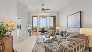 A spacious living room with a sofa, armchairs, a coffee table, and a ceiling fan. There is a large window offering a view of the outdoors. - Palm Harbor Penthouse With Marina Views 2 Bedroom Condo by RedAwning (Fort Myers Beach)