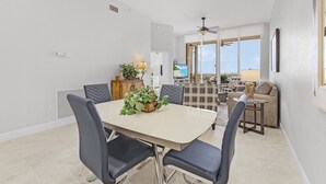 A modern dining area with a table and chairs, a plant centerpiece, and a view of the outdoor balcony. - Palm Harbor Penthouse With Marina Views 2 Bedroom Condo by RedAwning (Fort Myers Beach)