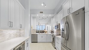 A modern kitchen with stainless steel appliances, white cabinetry, and a central island. - Palm Harbor Penthouse With Marina Views 2 Bedroom Condo by RedAwning (Fort Myers Beach)