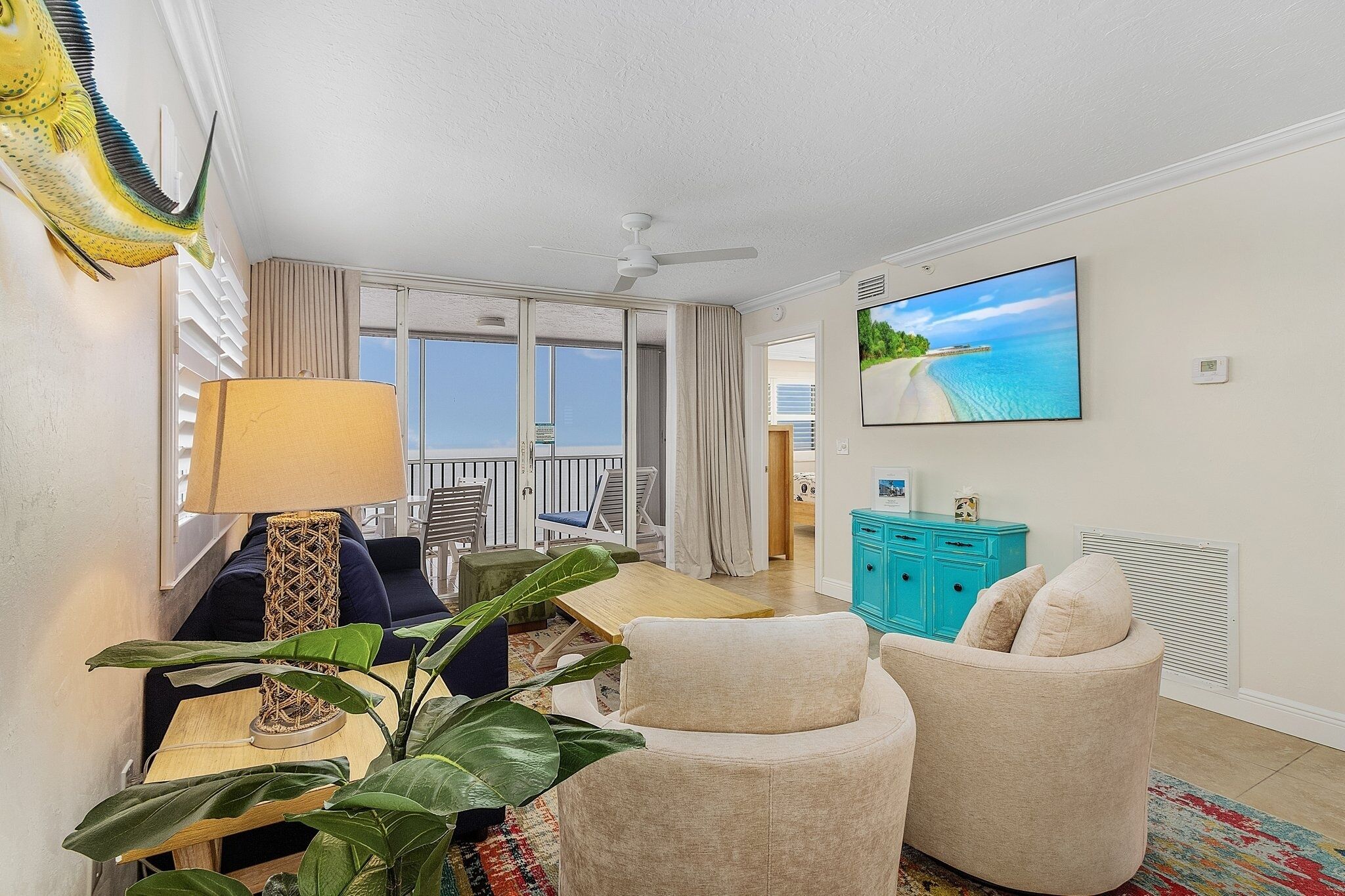 A living room with a sofa, a table, a lamp, a TV, and a view of the ocean.