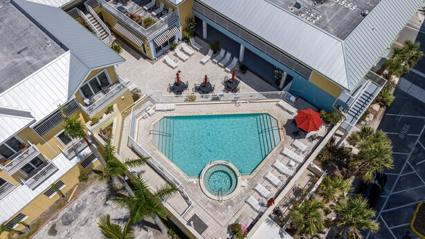 An aerial view of a hotel with a central swimming pool surrounded by lounge chairs and umbrellas, a covered patio area, and a parking lot. - Harbour House At The Inn Unit 211 1 Bedroom Condo by RedAwning (Fort Myers Beach)