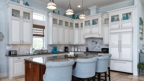 A spacious kitchen with white cabinetry, a large island with bar stools, pendant lighting, and a backsplash with a mosaic tile pattern. - Beautiful Home With Private Pool On The North End Of Fort Myers Beach! 4 Bedroom Home by RedAwning (Fort Myers Beach)
