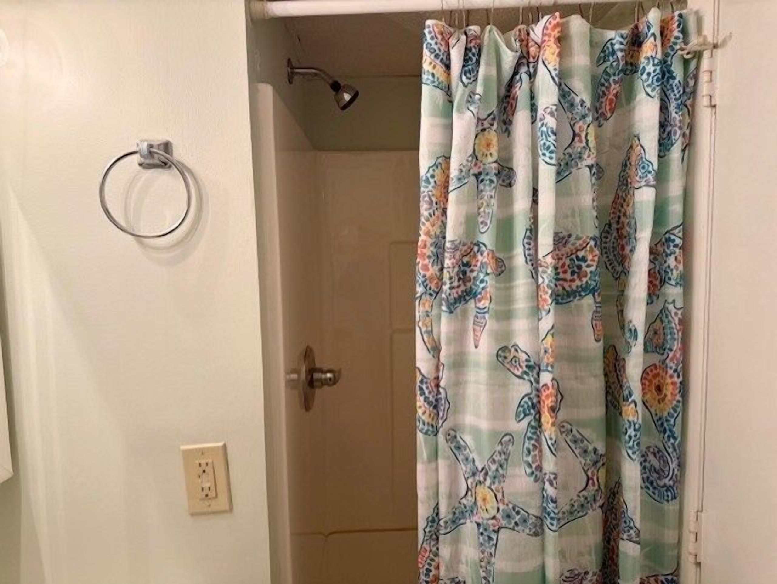 A bathroom with a shower curtain featuring a colorful pattern, a towel ring on the wall, and a door with a handle.