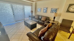 A living room with a sofa, coffee table, and a chair. There are two paintings on the wall and a clock. - Spectacular 2 Bedroom Condo on Sandy Beach at Las Palmas Resort G-201 2 Condo by RedAwning (Puerto Peñasco)