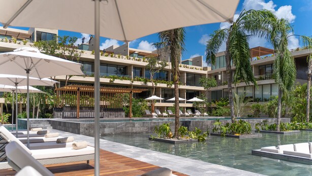 Ein Poolbereich eines Resorts mit Liegestühlen, Sonnenschirmen und einem modernen Gebäude mit Balkonen.