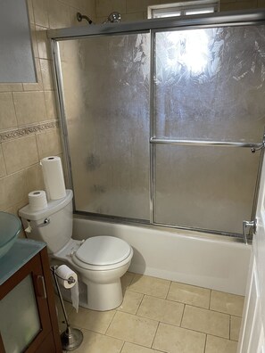A compact bathroom with a toilet, glass-enclosed shower stall, and decorative tile border.