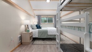 Un dormitorio con una cama litera, una mesita de noche con lámpara, una ventana con cortinas y una alfombra estampada.