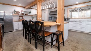 Una cocina con una isla central, vigas de madera, armarios blancos y un refrigerador de acero inoxidable.