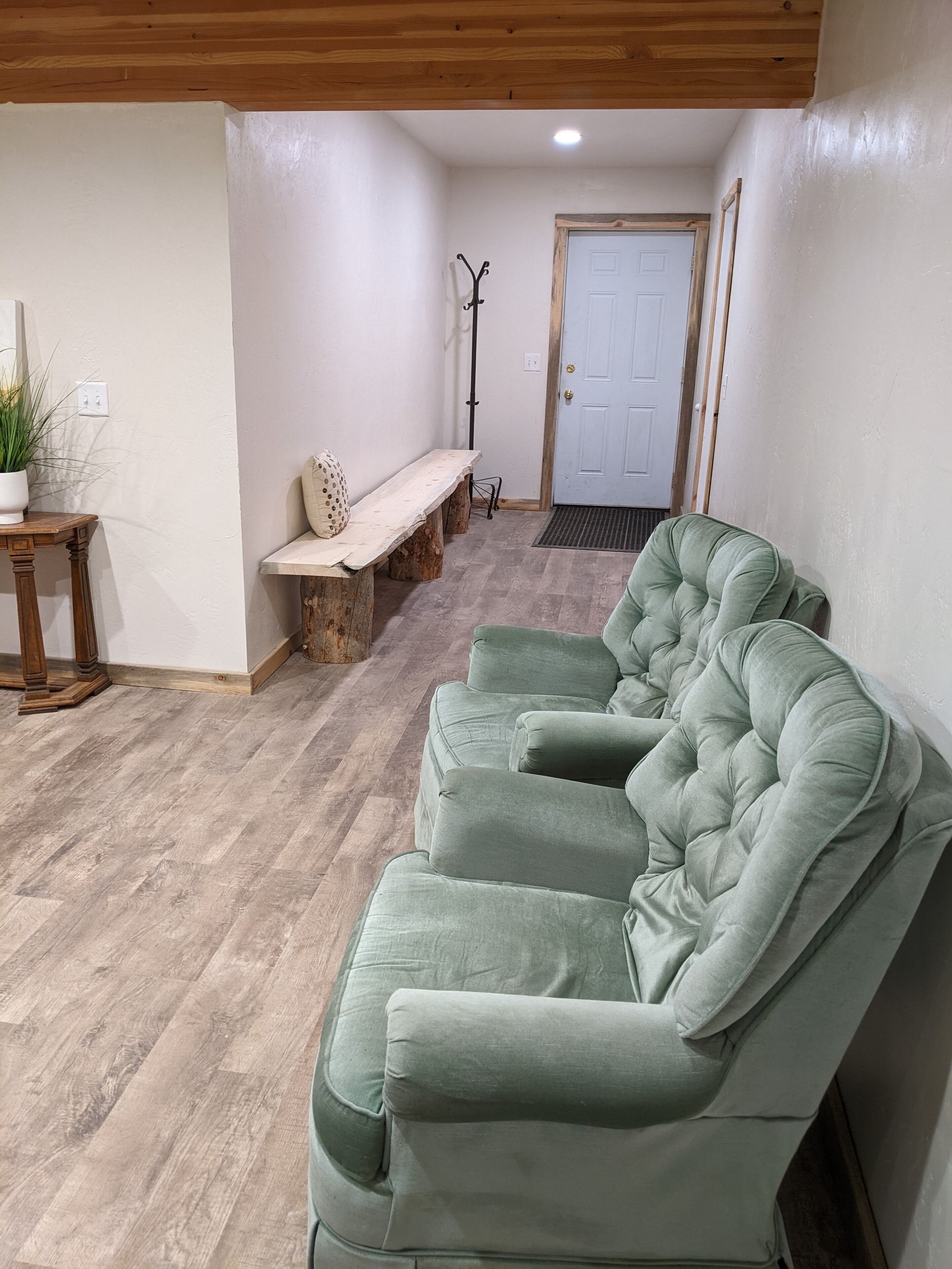 Ein Zimmer mit einem grünen Sofa, einer hölzernen Bank, einem Blumentopf und einer Tür im Hintergrund.