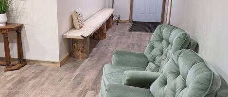 Ein Zimmer mit einem grünen Sofa, einer hölzernen Bank, einem Blumentopf und einer Tür im Hintergrund.