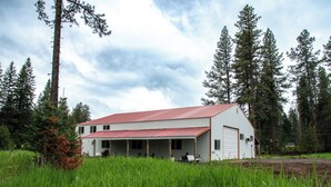 Un edificio blanco con tejado rojo, rodeado de árboles altos y césped verde.