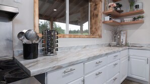 Una cocina con armarios blancos, encimera de mármol y estantes de madera.