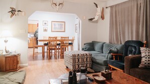 Una sala de estar acogedora con un sofá verde, una mesa de comedor de madera y sillas. Se observan adornos de pájaros en la pared y un ventilador de techo.
