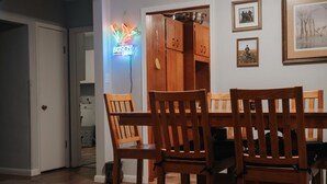 Un comedor con sillas de madera y una mesa, un letrero de neón, armarios de madera y cuadros en la pared.