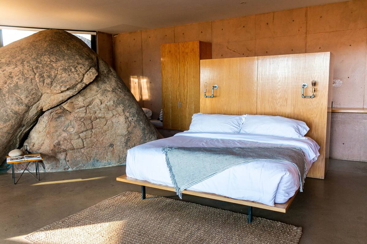Une chambre avec un grand rocher, une armoire en bois et un lit avec une literie blanche.