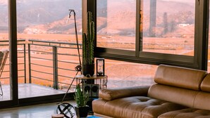 Een moderne woonkamer met een leren bank, een salontafel met tijdschriften, een cactus en uitzicht op een woestijnlandschap door grote ramen.