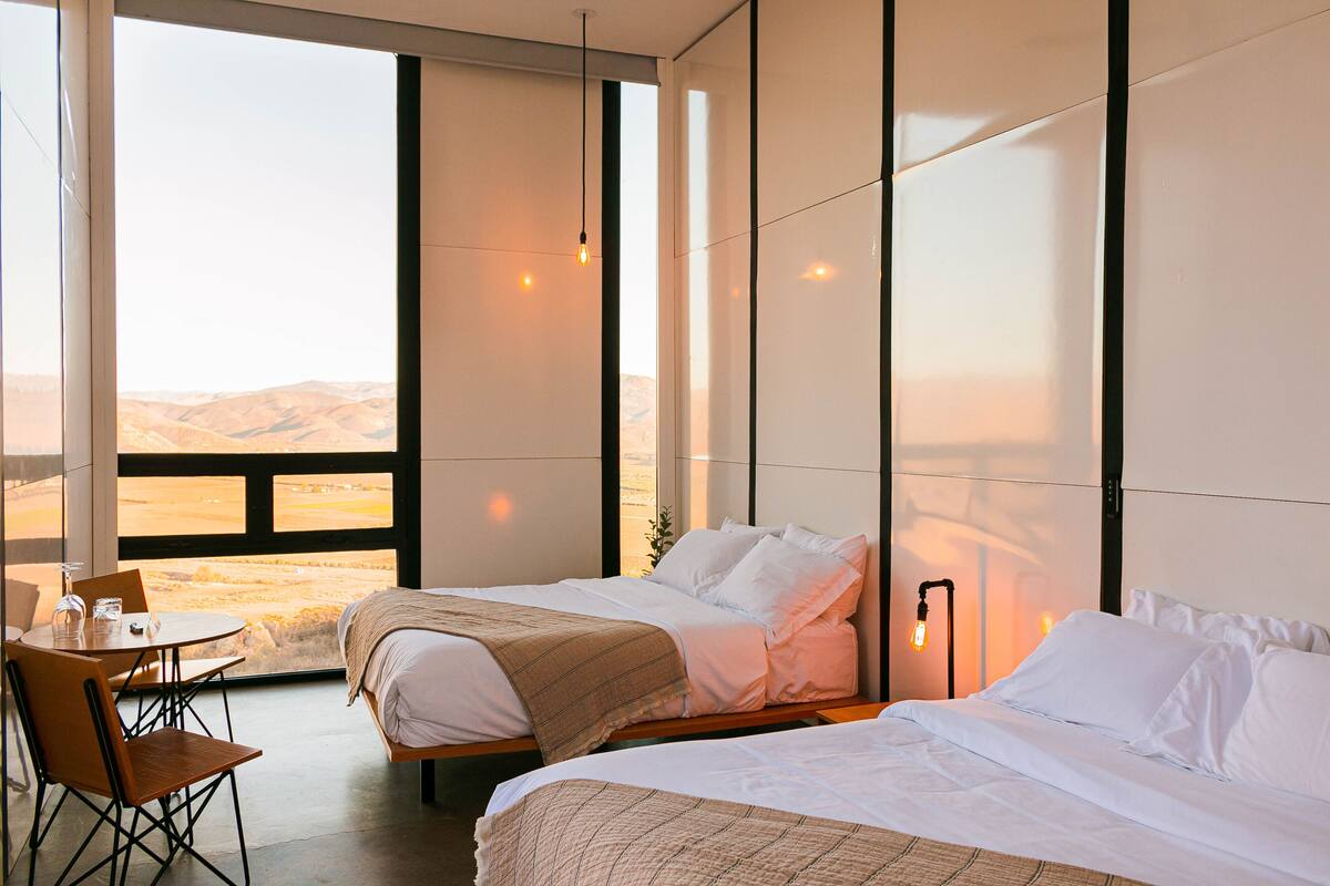 Une chambre d’hôtel avec deux lits, un coin repas comprenant une table et des chaises, et une grande fenêtre donnant sur le paysage.