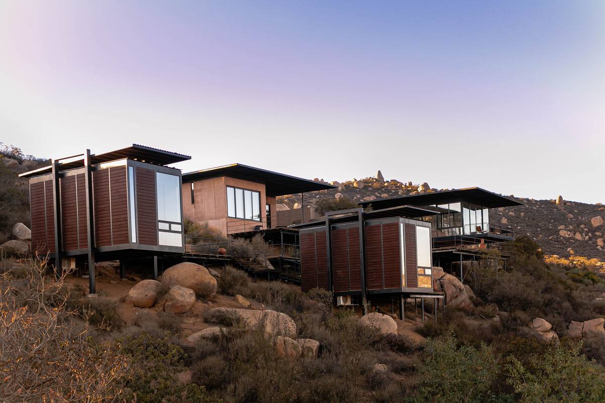 Un bâtiment moderne à plusieurs étages, doté de grandes fenêtres et d’un toit plat, situé dans un paysage rocheux et vallonné.