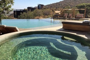 Une magnifique piscine à débordement aux eaux cristallines, dotée d’une terrasse en bois et de chaises longues, le tout entouré d’un paysage montagneux.