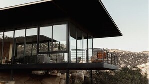 Een modern gebouw met grote glasramen, een plat dak en een balkon met uitzicht op een rotsachtig landschap.